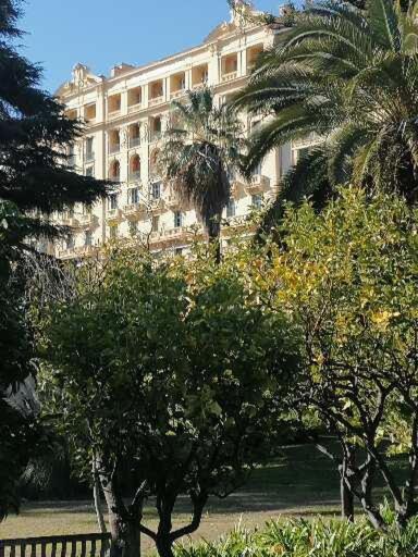 un grand bâtiment avec des palmiers devant dans l'établissement IMPERIAL PALACE Bord de Mer, à Menton
