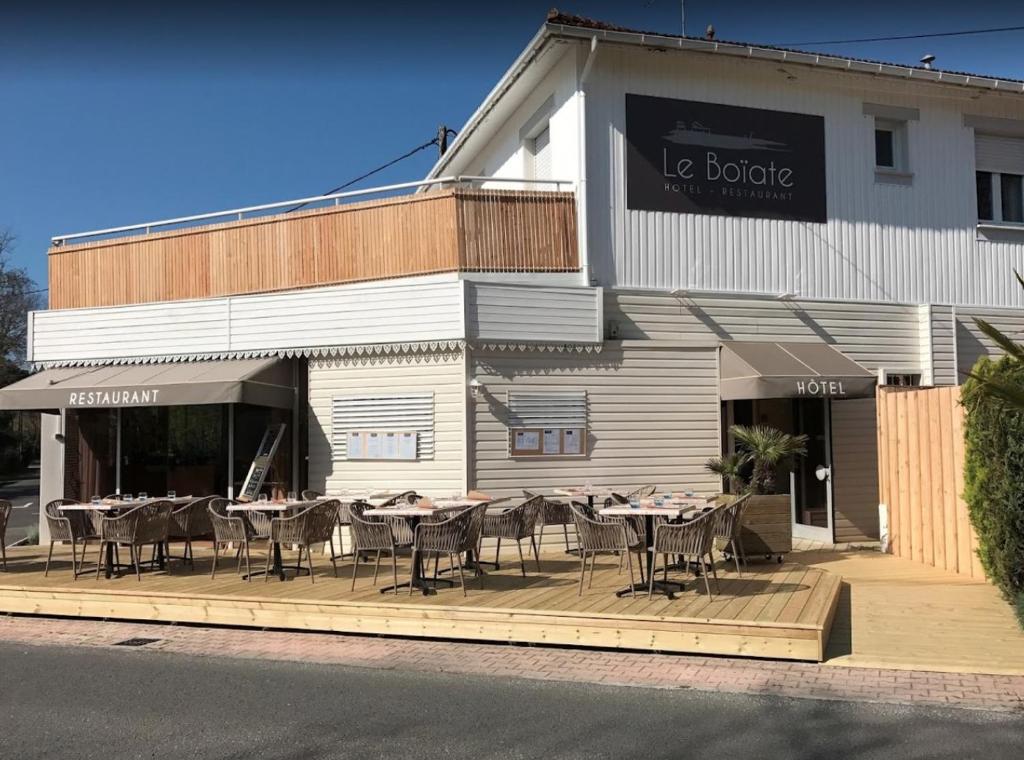 un restaurant avec des tables et des chaises en face d'un bâtiment dans l'établissement Hôtel Le Boïate, à Arès