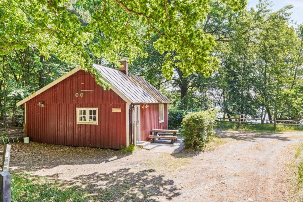 eine rote Scheune mit einer Bank neben einer unbefestigten Straße in der Unterkunft Fiskestugan – Country side cottage by lake in Sjöbo