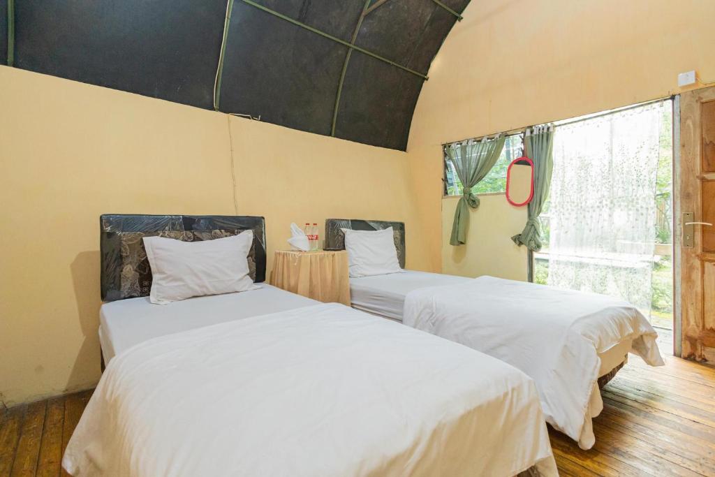 Junggo的住宿－Chikar Glamping At Wisata Coban Talun Mitra RedDoorz，一间卧室设有两张带白色床单的床和窗户。