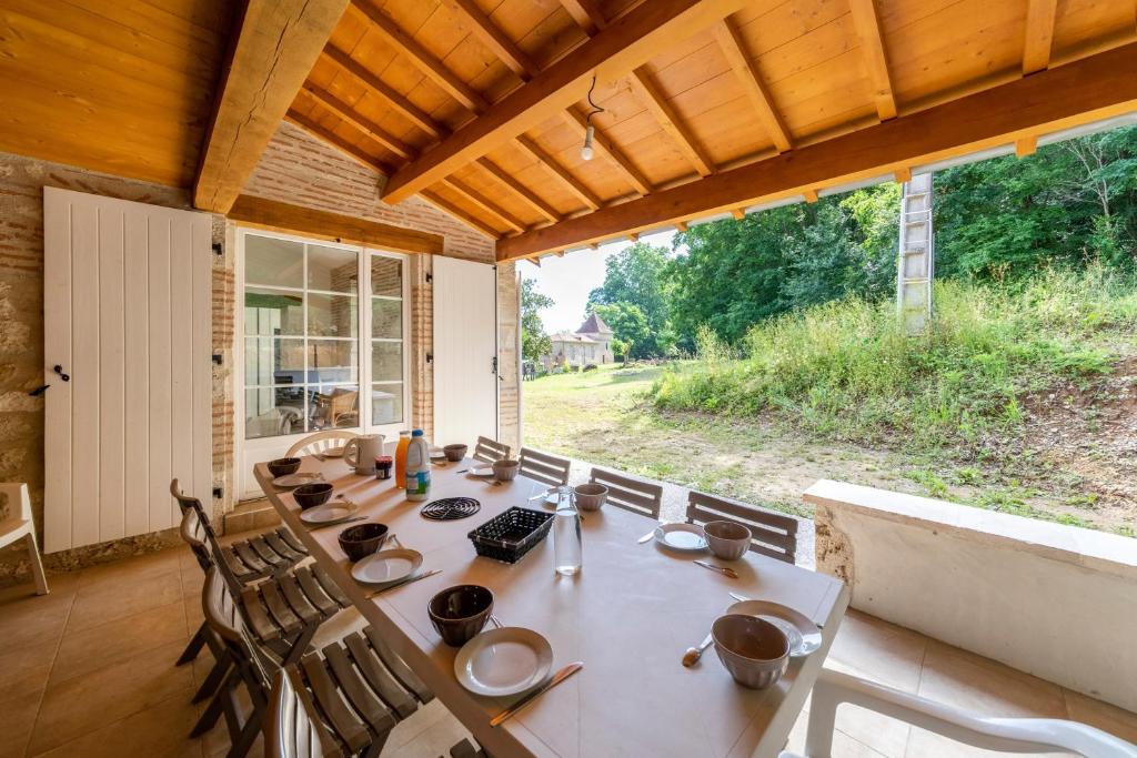 a dining room with a long table and a large window at La maison dans la nature - Cadre exceptionnel au bord de cours deau in Sainte-Livrade-sur-Lot