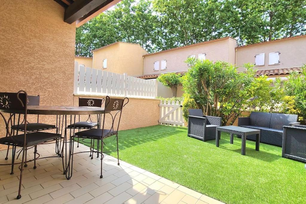 un patio avec une table, des chaises et de l'herbe dans l'établissement Proche plage - Pavillon de vacances Ohana & jardin - Richelieu, au Cap d'Agde
