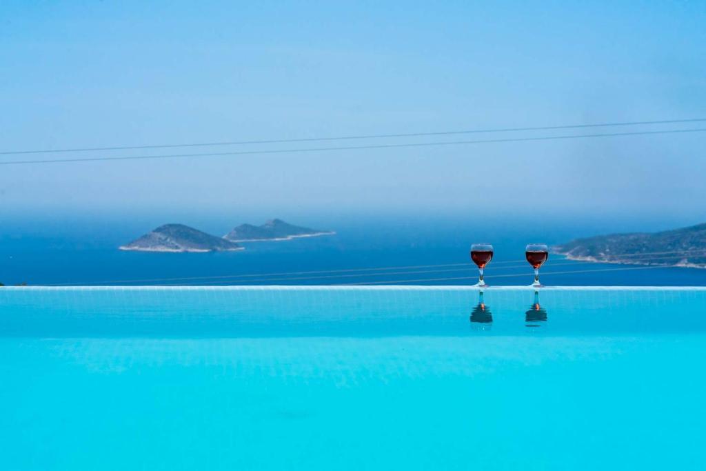 two glasses of wine sitting on the edge of the ocean at KaşKalkan Honeymoon Villa with Seaview in Kalkan