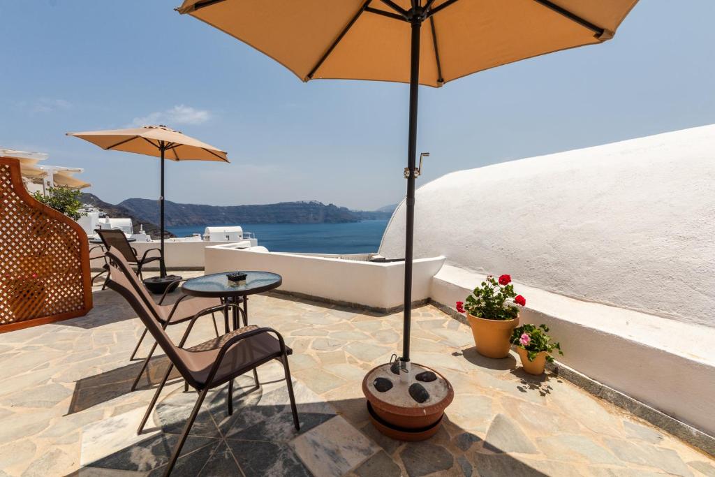 eine Terrasse mit einem Tisch, Stühlen und einem Sonnenschirm in der Unterkunft Ostria Caldera Studios in Oia