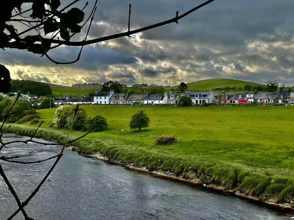 a river in a field with houses in the background at Apple Cottage in Newton Stewart