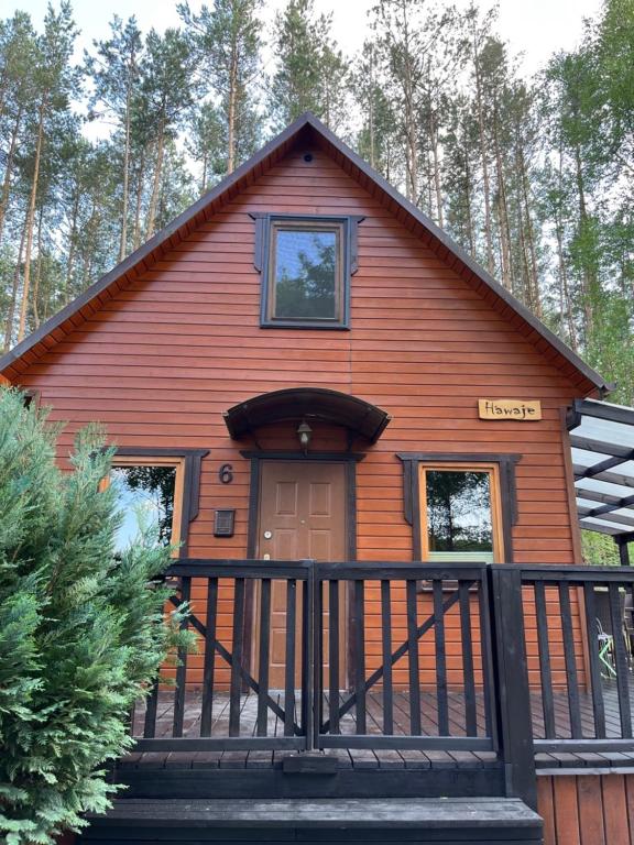 ein rotes Haus mit einer Veranda mit einem Zaun in der Unterkunft Domek całoroczny HAWAJE nad jeziorem Kazub in Cieciorka