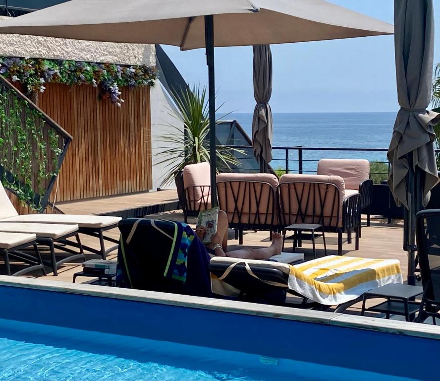 - une piscine avec des chaises et un parasol et l'océan dans l'établissement Les Alcyons, au Lavandou