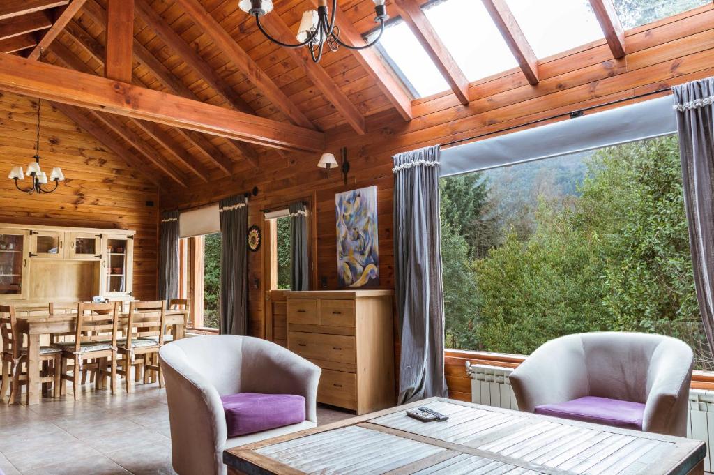 a living room with a table and chairs and a large window at BOG Melania - casa en el bosque in Villa La Angostura