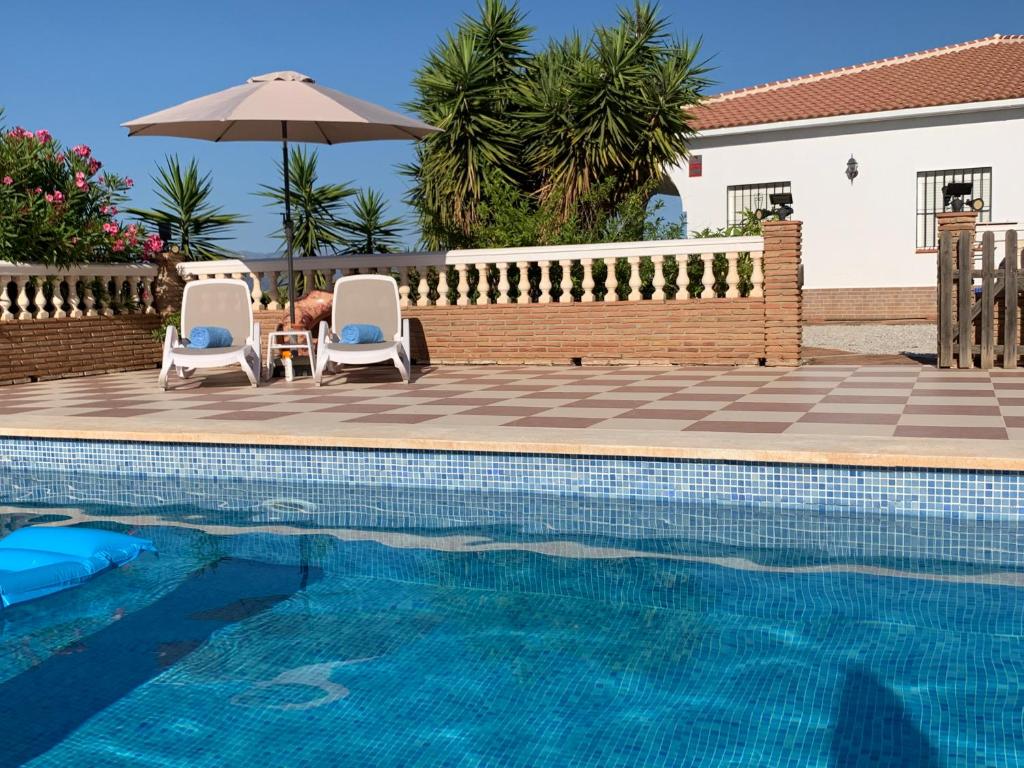 uma piscina com duas cadeiras e um guarda-sol em Casa Anhelando Andalucia - Een villa prachtig op een heuveltop met magnifiek uitzicht nabij dorp en strand em Iznate