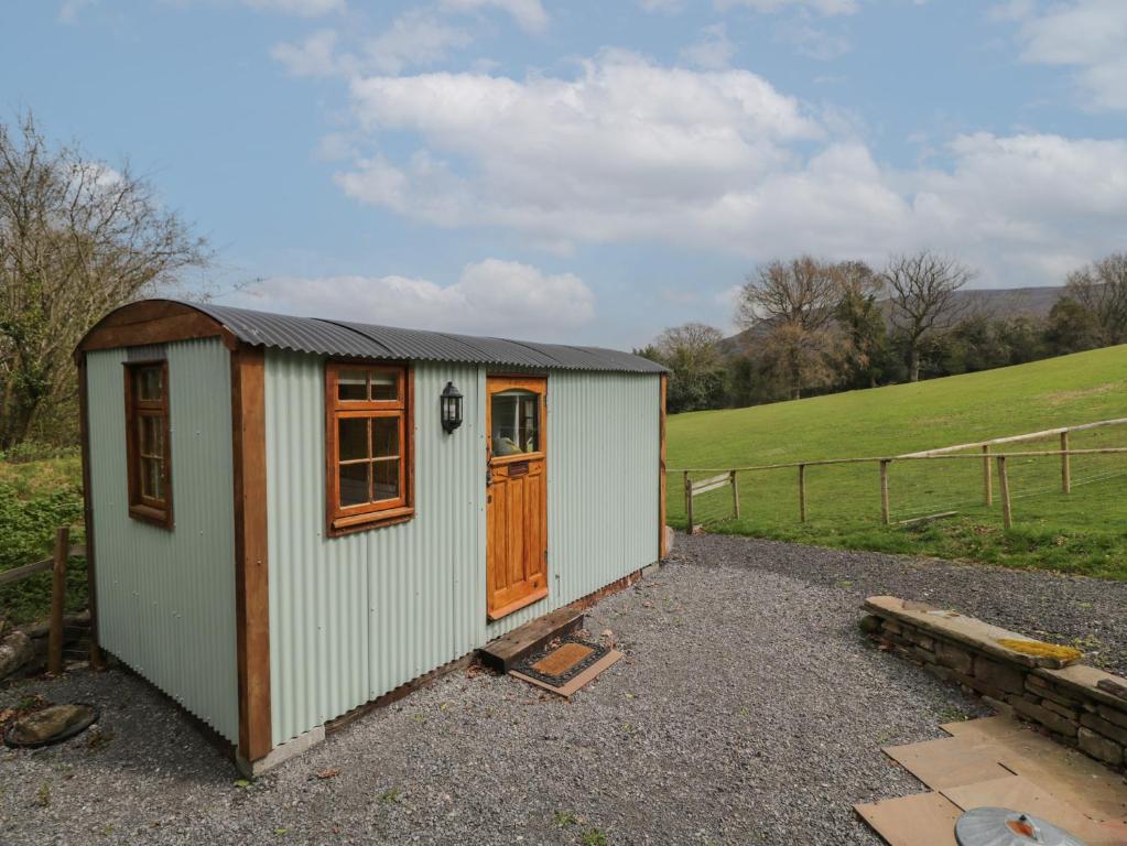 un pequeño cobertizo con una puerta de madera en un campo en Rabbit Hill Hut, en Abergavenny