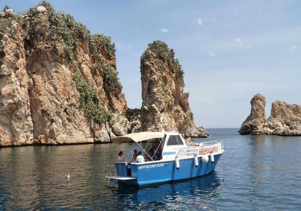 a blue and white boat in the water near some rocks at Appartamento Valentina in San Vito lo Capo