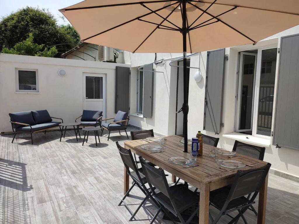 - une table en bois avec des chaises et un parasol sur la terrasse dans l'établissement Maison au calme avec parking proche centre-ville, à Orange