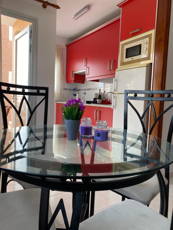 a glass table in a kitchen with red cabinets at Seaside apartment with balcony in Las Galletas