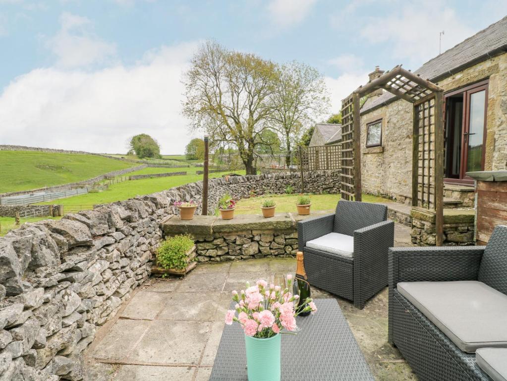 eine Terrasse mit einer Steinmauer, Stühlen und Blumen in der Unterkunft Clover Cottage at Pikehall in Matlock