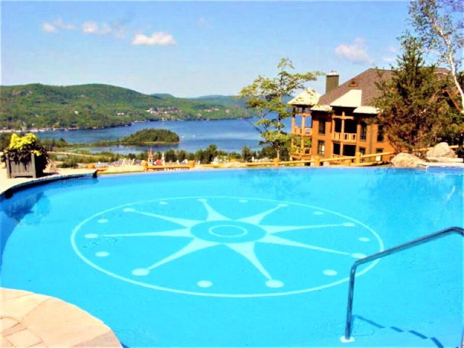 una gran piscina azul con vistas al lago en Équinoxe 164-2 / Exclusive Mountain Home With View, en Mont-Tremblant