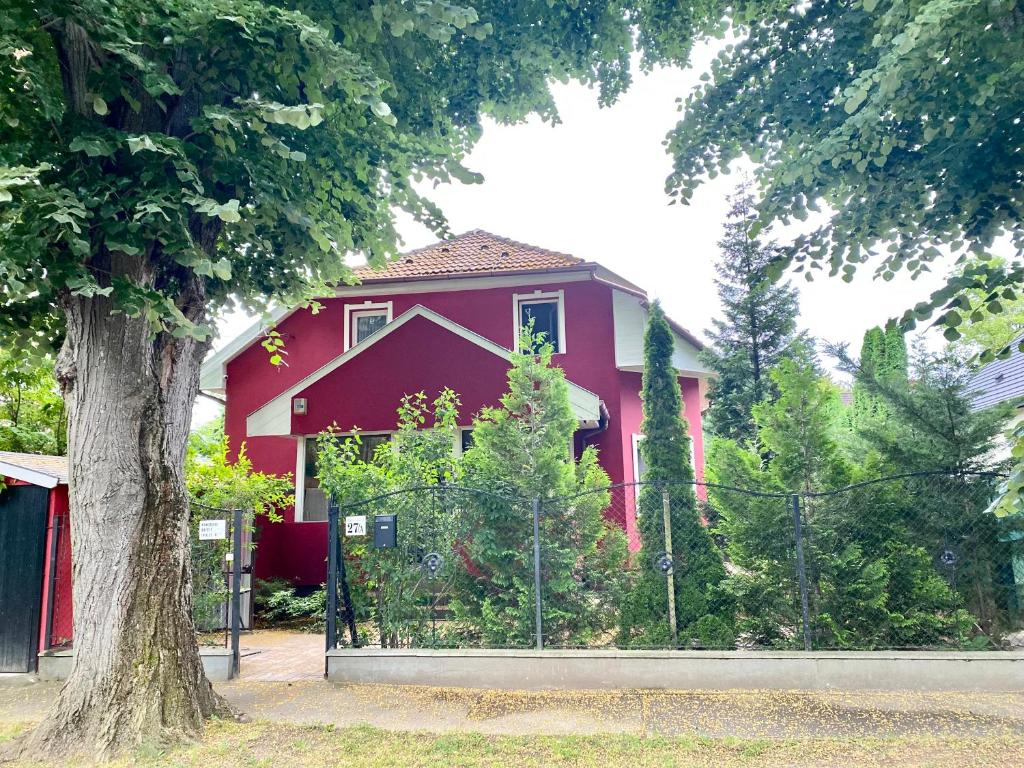 ein rotes Haus mit einem Zaun davor in der Unterkunft Nyugalom Szigete in Balatonszemes