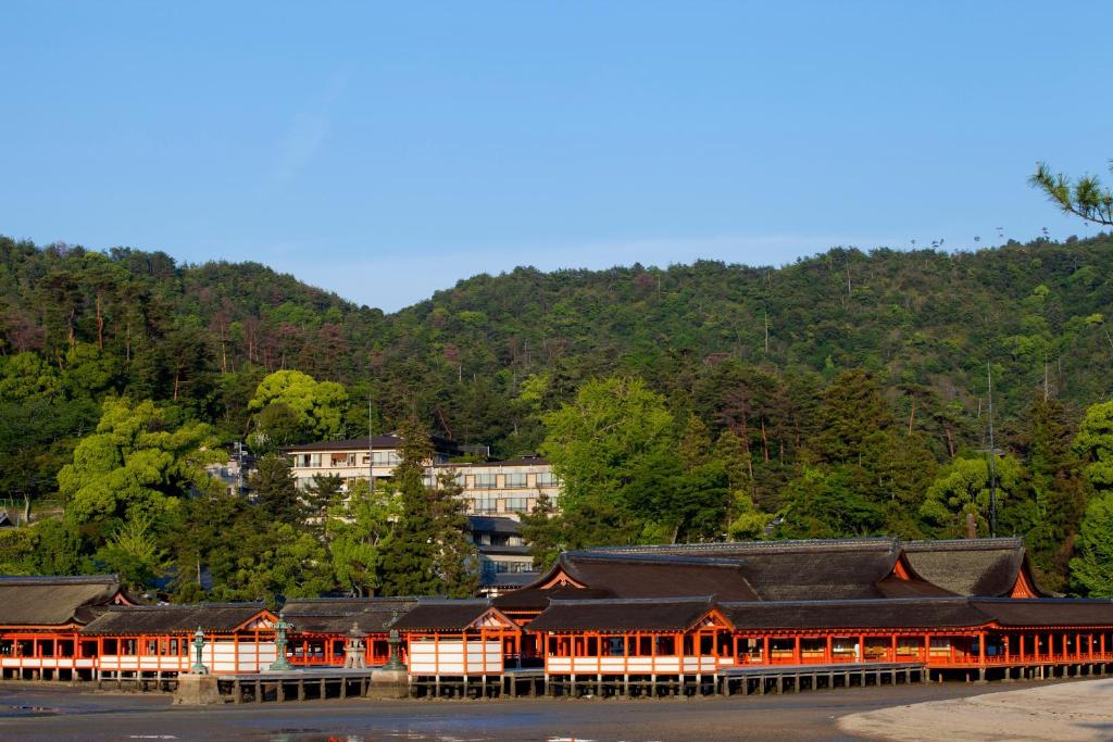 a group of buildings on the water with a mountain at Miyajima Grand Hotel Arimoto in Miyajima