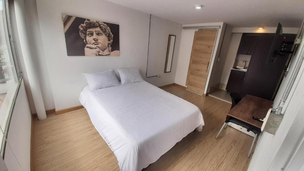 Un dormitorio con una gran cama blanca y una mesa en Apartaestudios Amoblados Galerías, en Bogotá