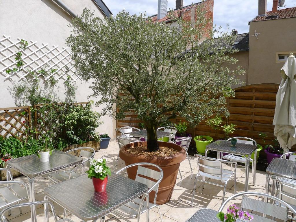 un patio con mesas, sillas y un árbol en Logis-Hôtel des Oliviers en Thionville