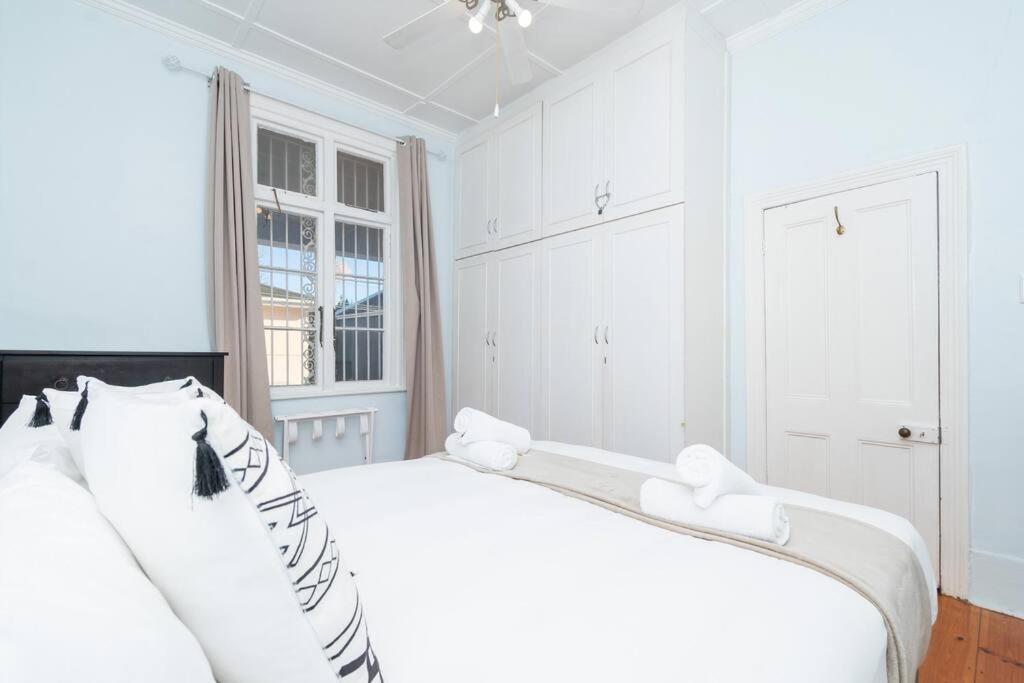 a white bedroom with two white beds and a window at Enchanting Abode in Rosebank in Cape Town