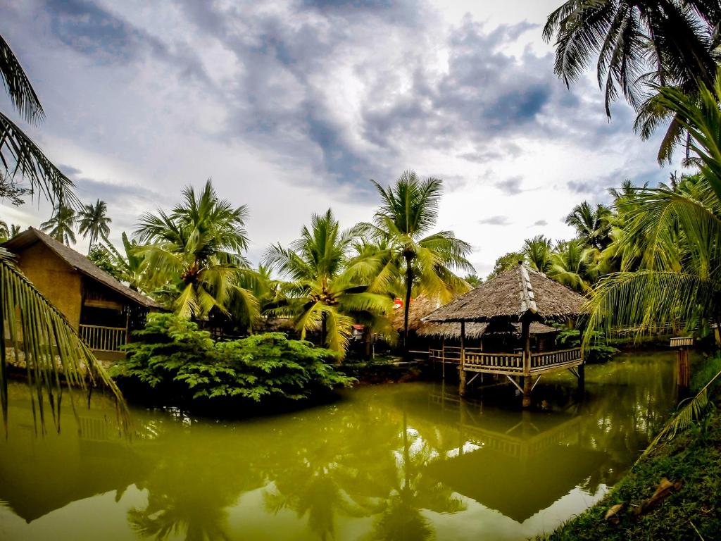 a resort with a pond with a gazebo and palm trees at Bale'ku in Pangandaran