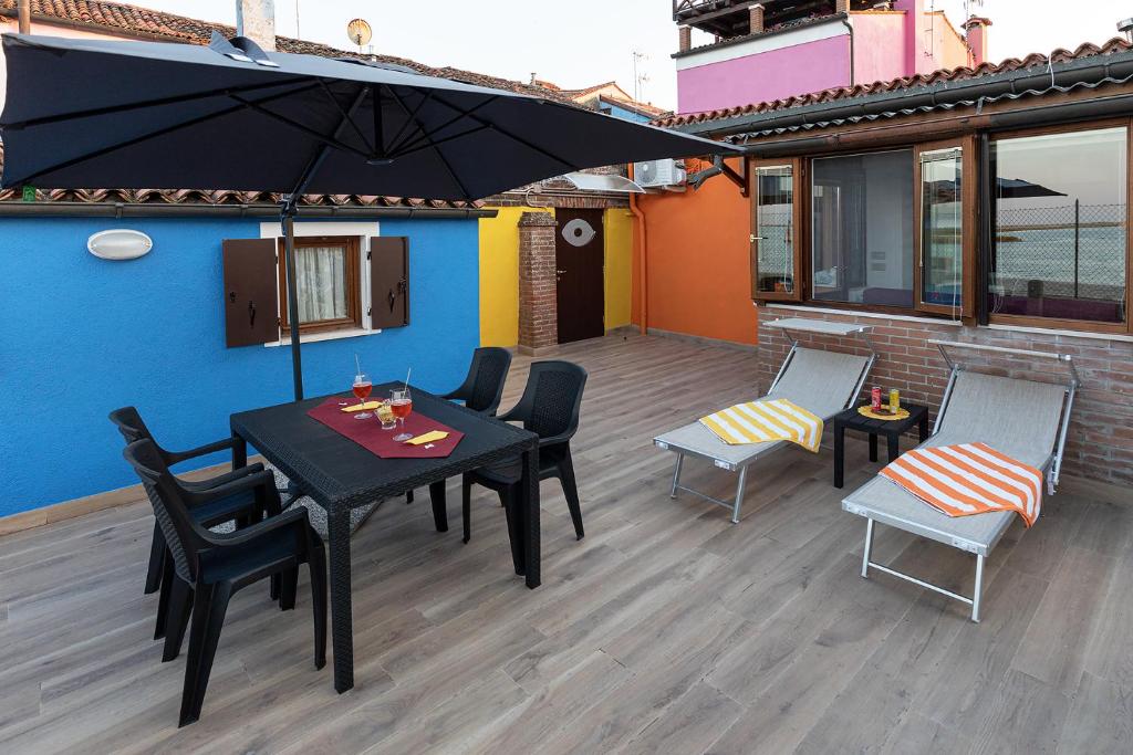een patio met een zwarte tafel en stoelen en een parasol bij Burano L' Occhio sulla Laguna in Burano