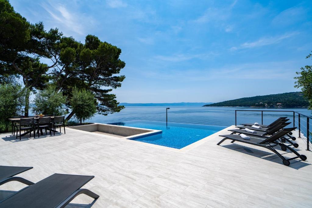a swimming pool with chairs and a table and water at Seaside luxury villa with a swimming pool Sumartin, Brac - 5639 in Sumartin