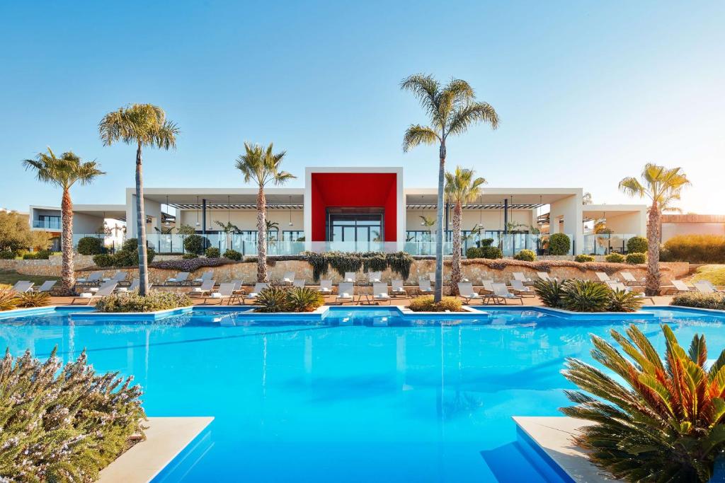 a swimming pool with palm trees and a building at Tivoli Alvor Algarve - All Inclusive Resort in Alvor