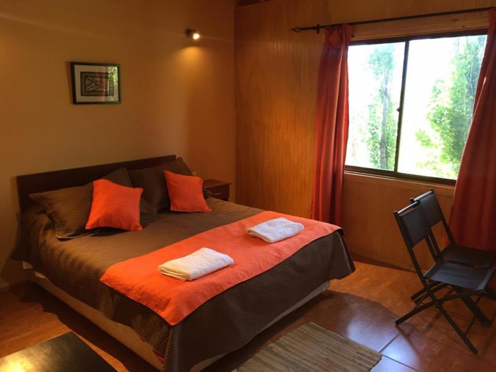 sypialnia z łóżkiem z pomarańczowymi poduszkami i oknem w obiekcie Patagonia Bordelago w mieście Puerto Ingeniero Ibáñez