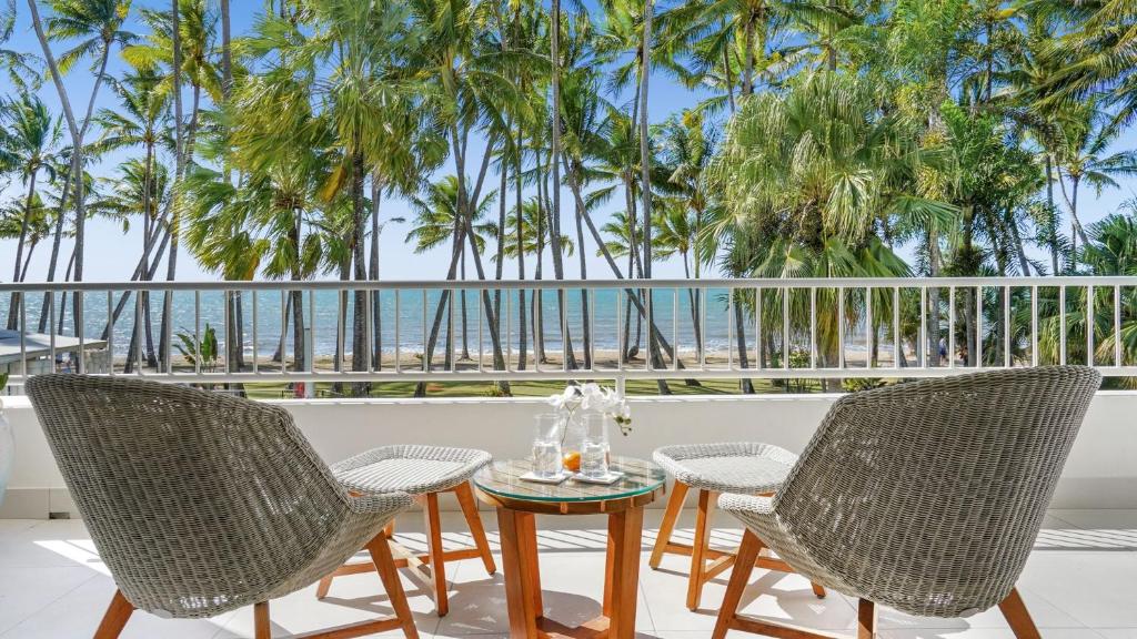 een tafel en stoelen op een balkon met uitzicht op het strand bij Belle Escapes presents 14 Alamanda Resort Where Pure Luxury meets the Coral Sea in Palm Cove