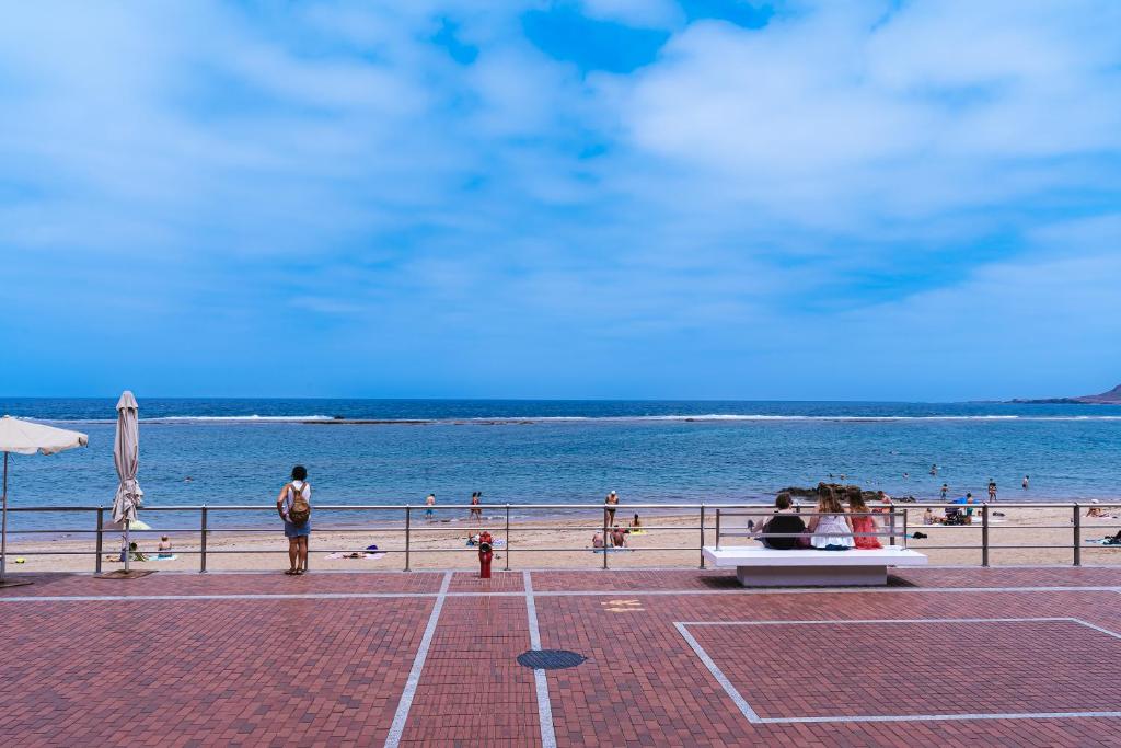 a beach with people sitting on a bench next to the ocean at 1linea Canteras in Las Palmas de Gran Canaria