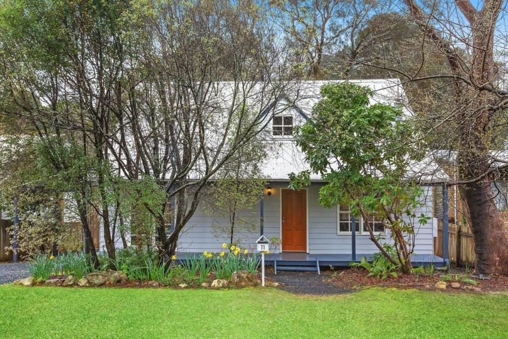 ein weißes Haus mit einer orangefarbenen Tür im Hof in der Unterkunft Bunyip Cottage in Katoomba