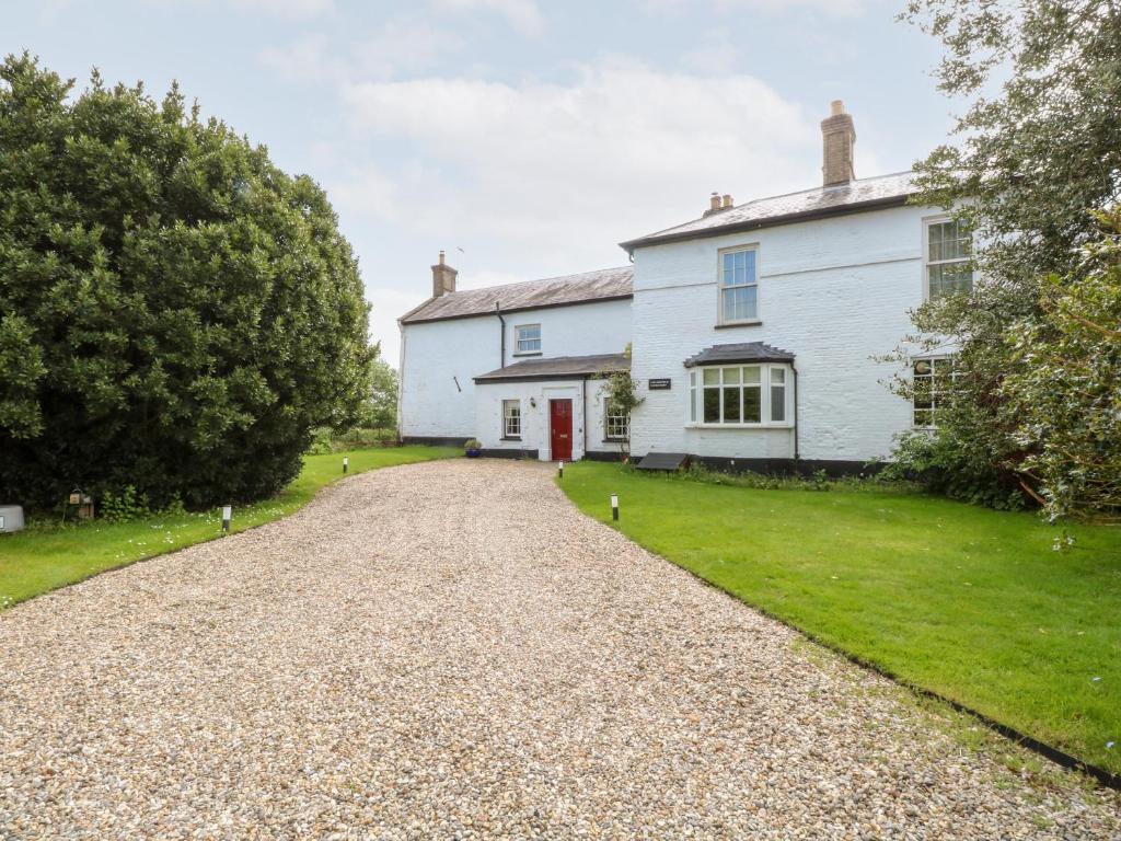 a white house with a red door on a gravel road at The Farmhouse in North Walsham