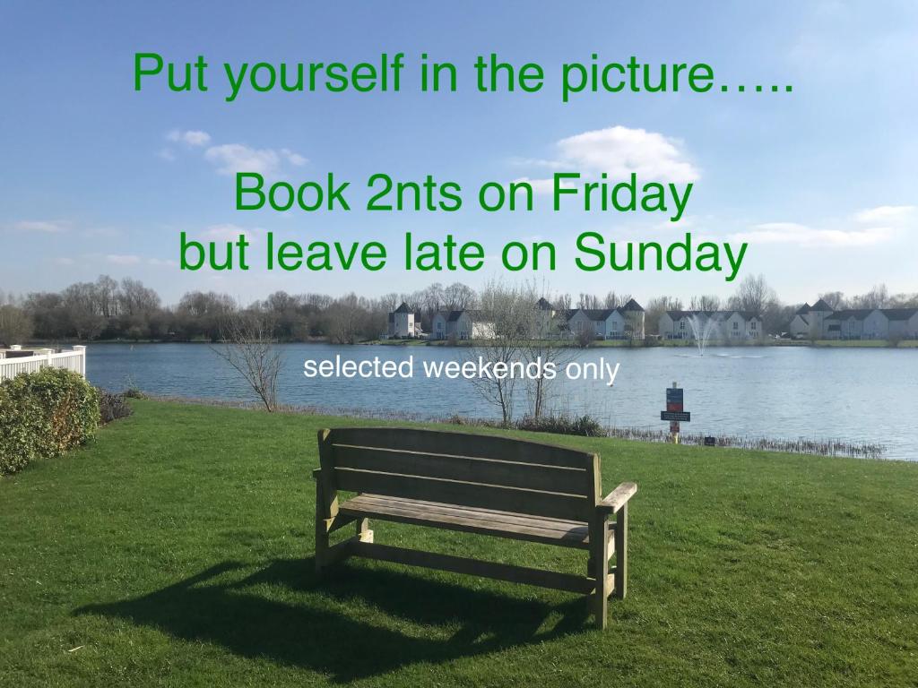 a park bench sitting in the grass next to a lake at Liming Lodge - Lakeside Home in the Cotswolds in South Cerney