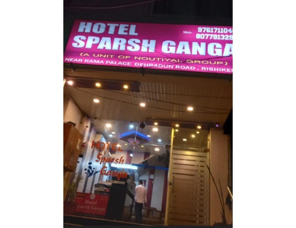 een man die voor een gebouw staat met een bord bij Hotel Sparsh Ganga, Rishikesh in Rishīkesh