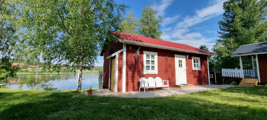 een rood huis met witte stoelen voor een meer bij Mysig stuga med sjötomt, nära Järvsöbacken in Järvsö