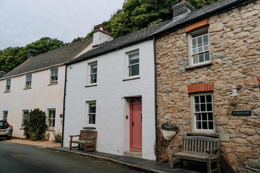 a white building with a red door and two benches at Cute and cosy 2 bed cottage in beautiful Solva in Solva