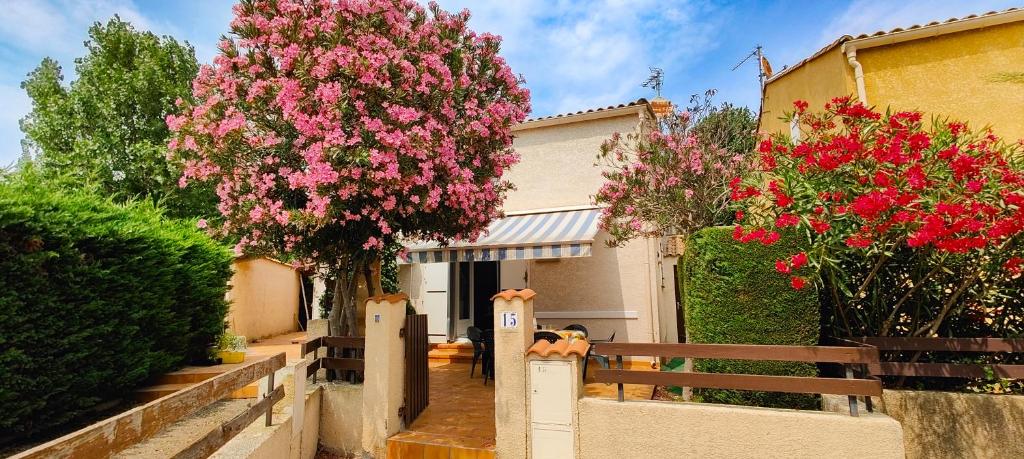une maison avec des fleurs roses devant une clôture dans l'établissement Maison de vacances climatisée à 600m de la plage, à Vias