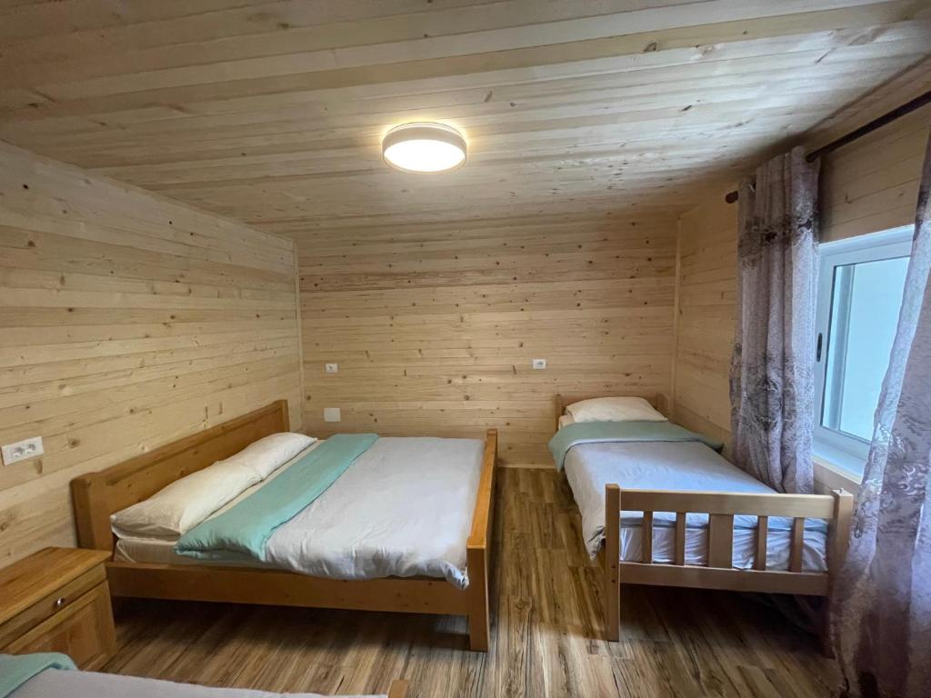 two beds in a log cabin with a window at Lazer Cardaku guest house in Valbonë