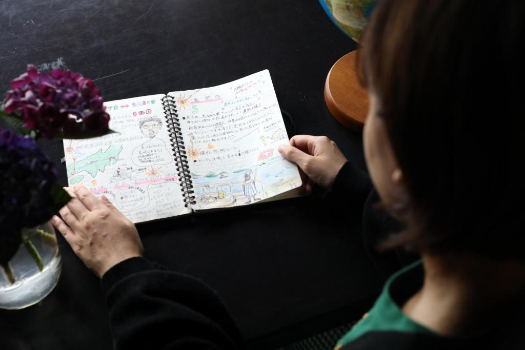 a woman sitting at a table reading a book at Guesthouse SETOUCHI LIFE in Kure