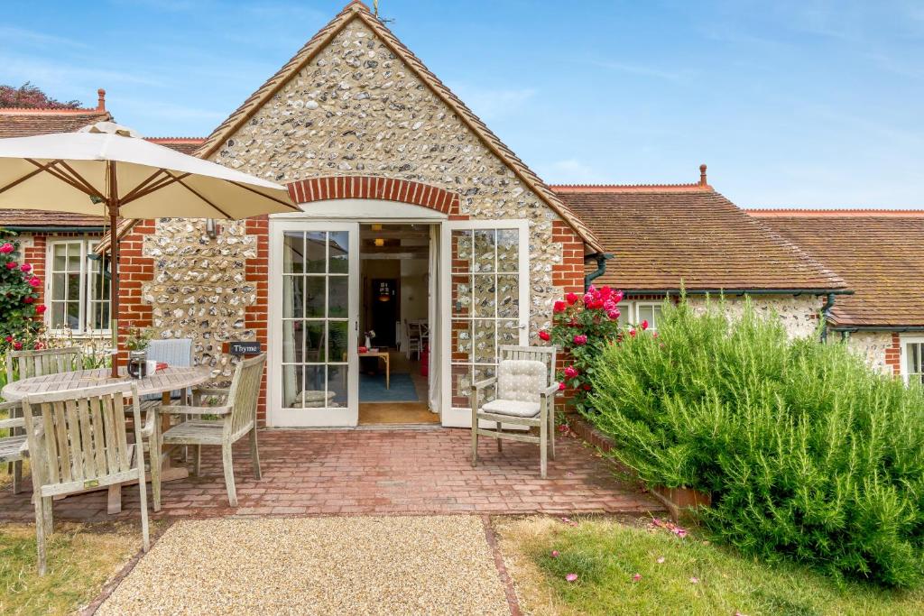 a brick house with a patio with an umbrella at Thyme Cottage in Eastdean