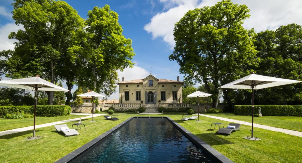 a pool in front of a house with umbrellas at Clos Marcamps - Teritoria in Prignac-et-Marcamps