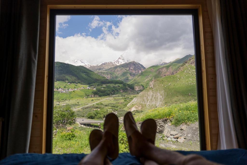 Gorai في كازباجي: شخص يستلقي على سرير وينظر من النافذة إلى الجبال