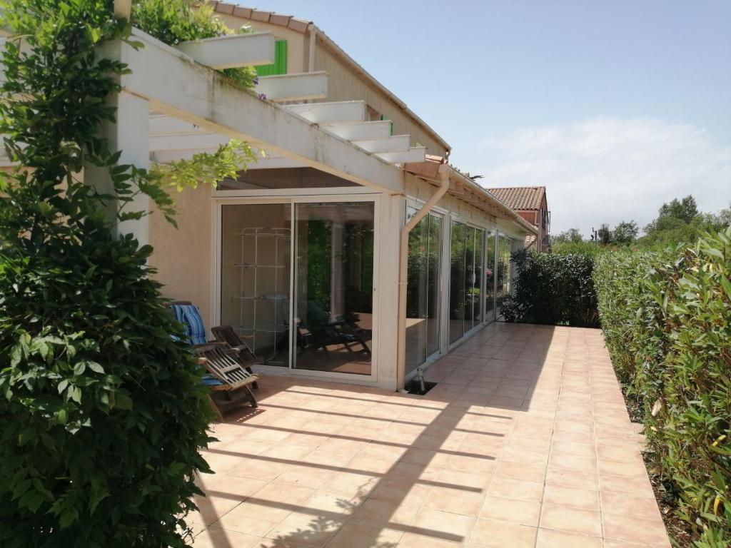 une terrasse d'une maison avec des portes en verre dans l'établissement Belle villa climatisée 3 chambres, véranda, terrasse arborée dans résidence sécurisée avec piscine commune 800m de la mer WIFI Un vrai Havre de Paix LRCS98, à Portiragnes