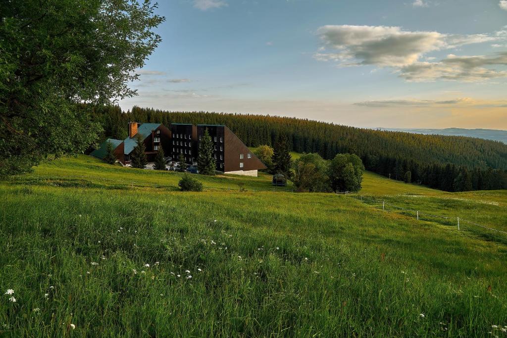 a barn on a hill with a field of grass at Hotel Tetřeví Boudy in Pec pod Sněžkou