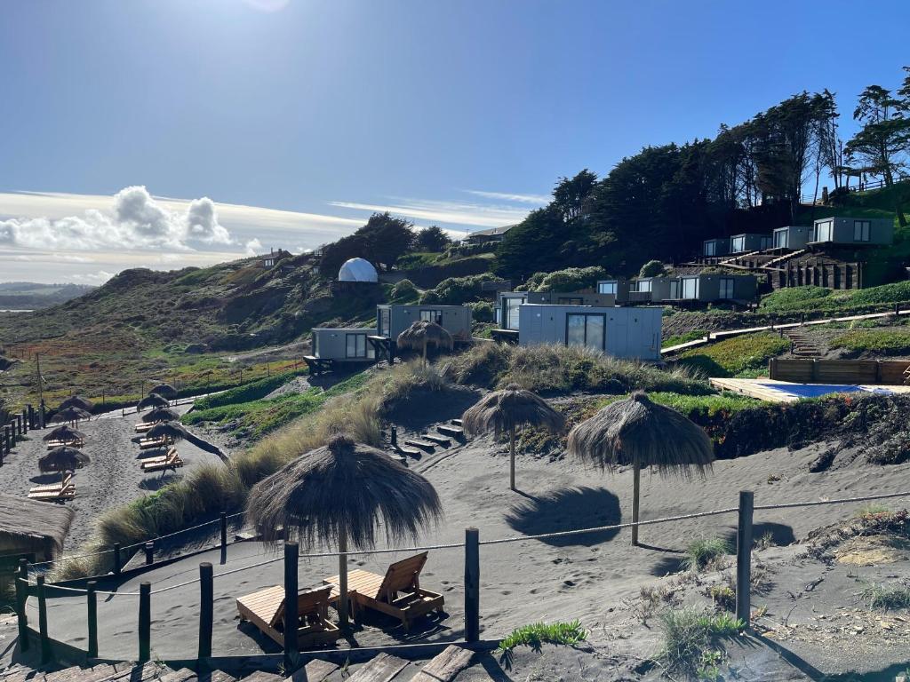 a beach with straw umbrellas and chairs on the sand at Recondito Lodge in Pichilemu