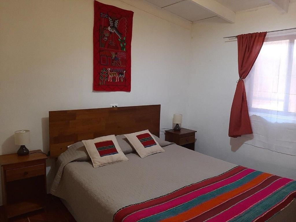 a bedroom with a bed with a colorful blanket and a window at Casa Sutar Los Pimientos in San Pedro de Atacama