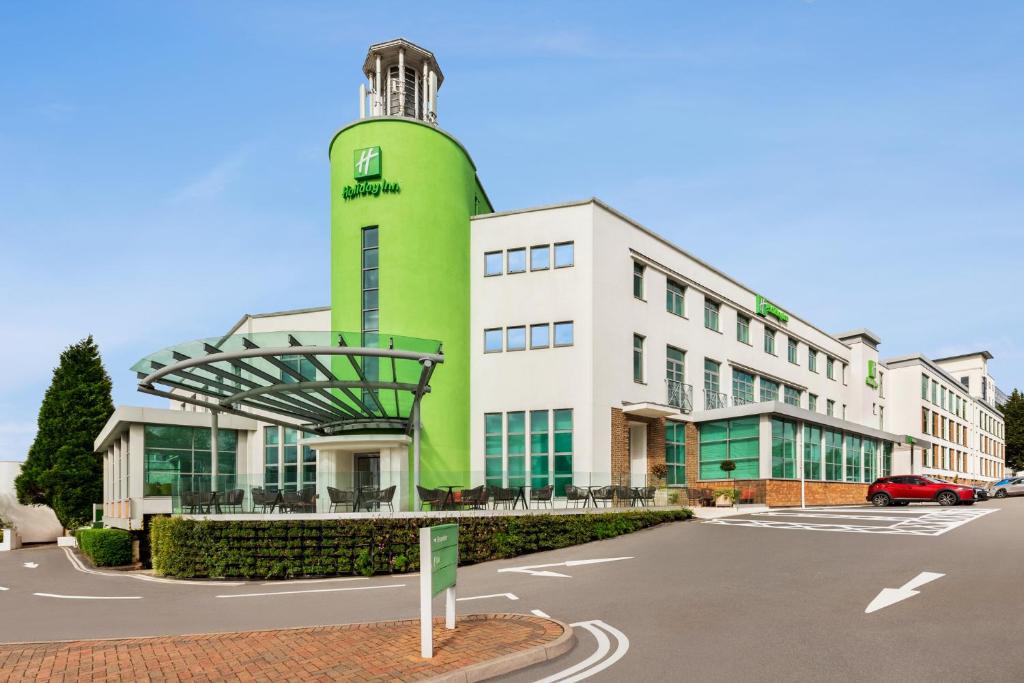 ein grünes Gebäude mit einem Uhrturm auf einem Parkplatz in der Unterkunft Holiday Inn Birmingham Airport - NEC, an IHG Hotel in Bickenhill
