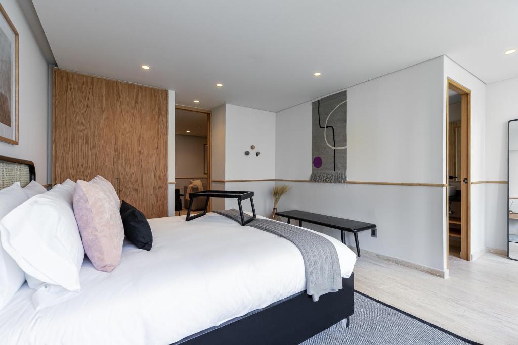 A spacious bedroom with a large bed, bench and adjoining doorway.