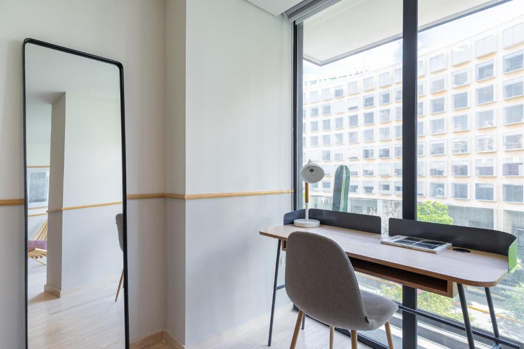 A compact desk beside a full-height window overlooking a nearby building.